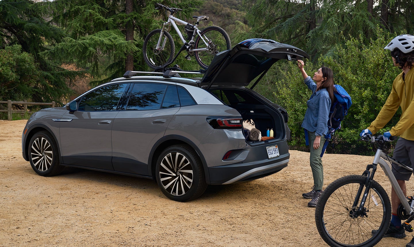 A man and woman load mountain bicycles onto a Pure Gray ID.4 Pro S Plus with cross bars and a bike attachment that’s parked in a natural, outdoor setting.